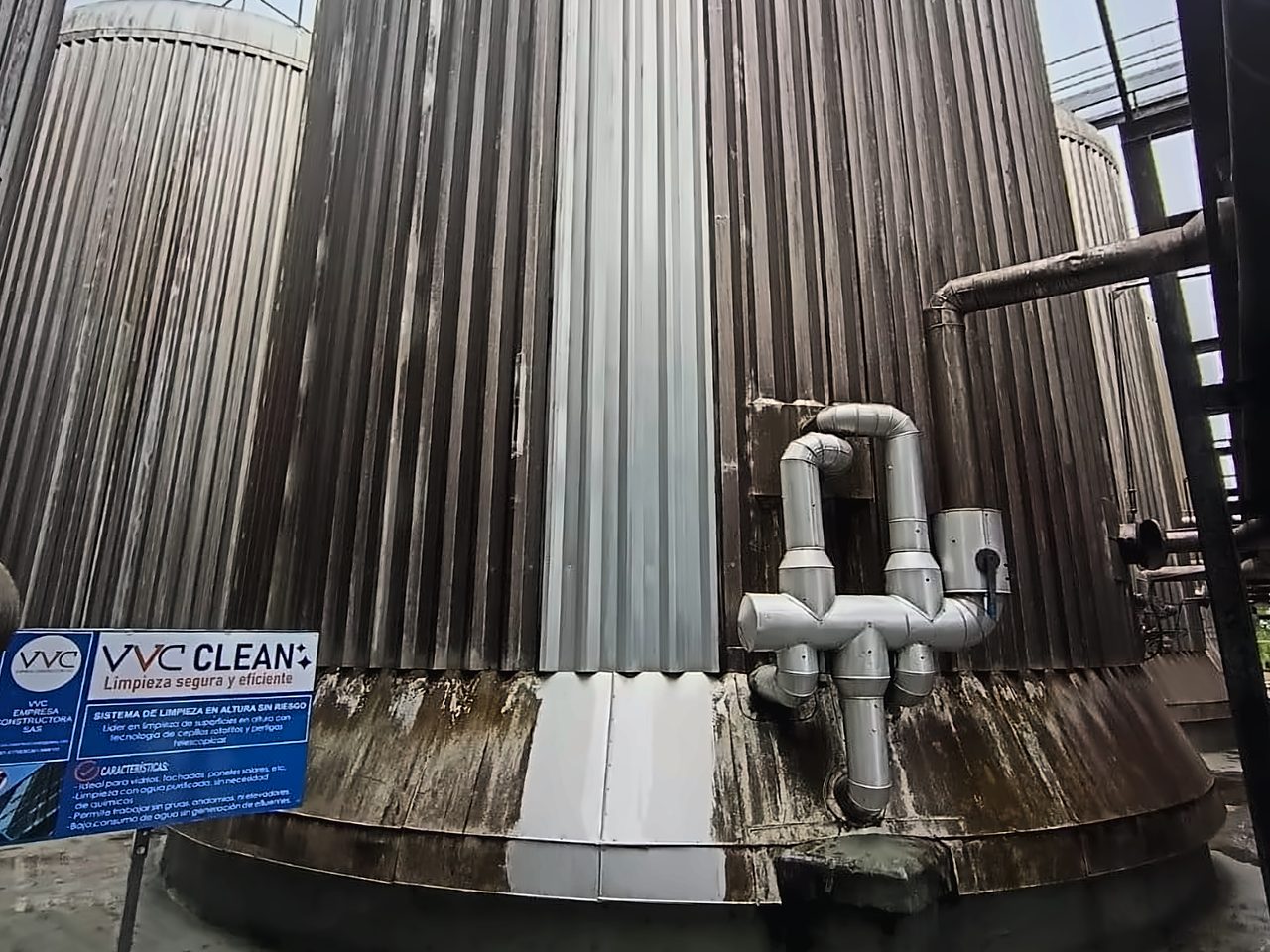 Tanque industrial con la franja recién limpiada junto al cartel de obra de VVC Clean: la chapa limpia contrasta con los paneles sucios.